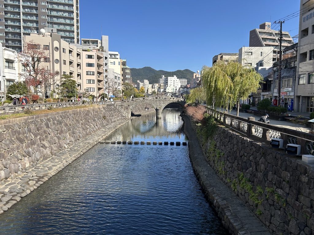 石橋が架かる川沿いの街並みと、その奥に広がる山々